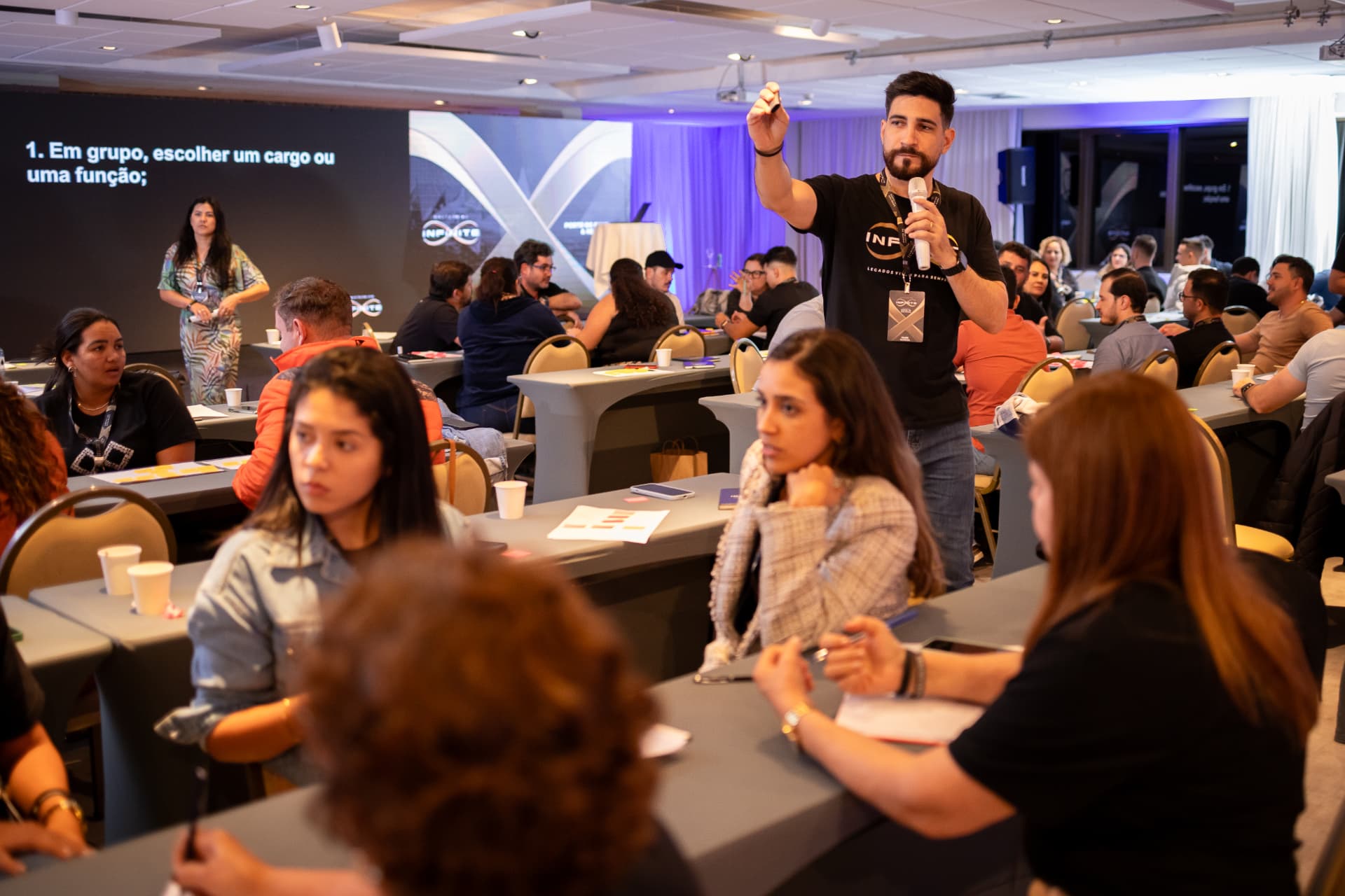 Encontro do Infinite: empresário apresentando com microfone diante dos participantes sentados às mesas